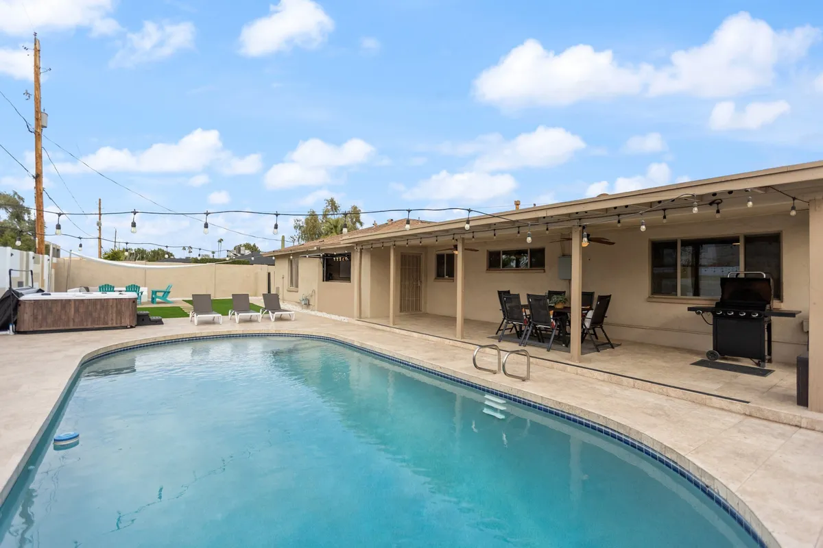 A vibrant outdoor space featuring a sparkling swimming pool, comfortable seating area, grill, and string lights overhead. The area exudes a leisurely, celebratory mood—ideal for gatherings after a day out at games or golf.
