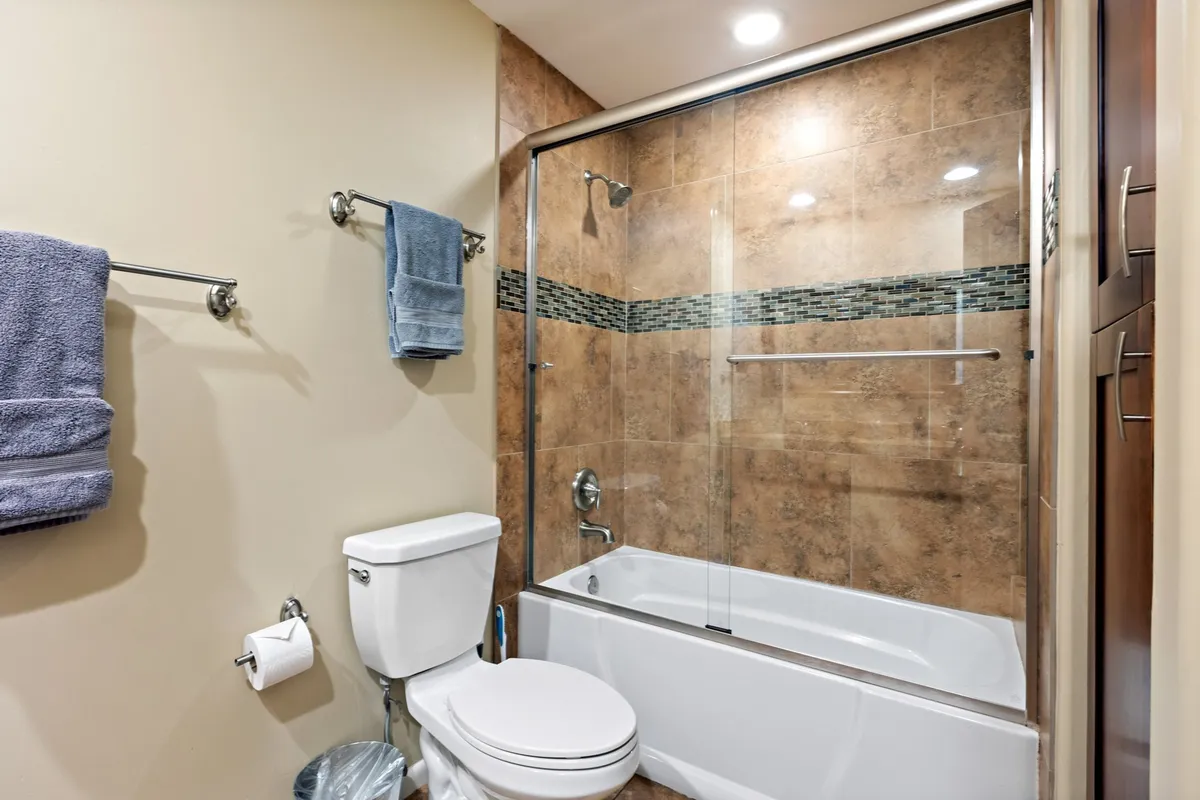 A modern bathroom with a glass shower enclosure, textured tile walls, fresh towels on racks, and contemporary fixtures. The space feels refreshing and serene, designed for both convenience and relaxation.