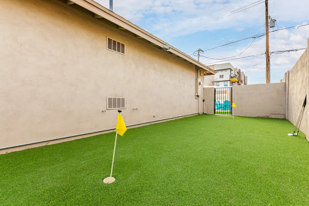 A lush artificial turf golf putting green with bright yellow flags offers a dedicated space for friendly competitions and outdoor fun. The scene is casual, inviting, and emphasizes recreation in a sun-drenched backyard setting.