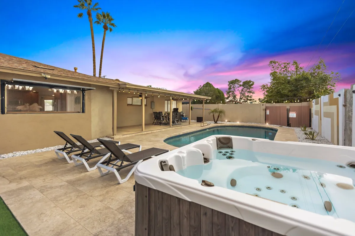 A vibrant exterior area with a swimming pool, hot tub, padded lounge chairs, and a patio surrounded by palm trees. The setup encourages relaxation and social gatherings, with the inviting water and comfortable seating taking center stage. The scene transitions beautifully from day to evening use.