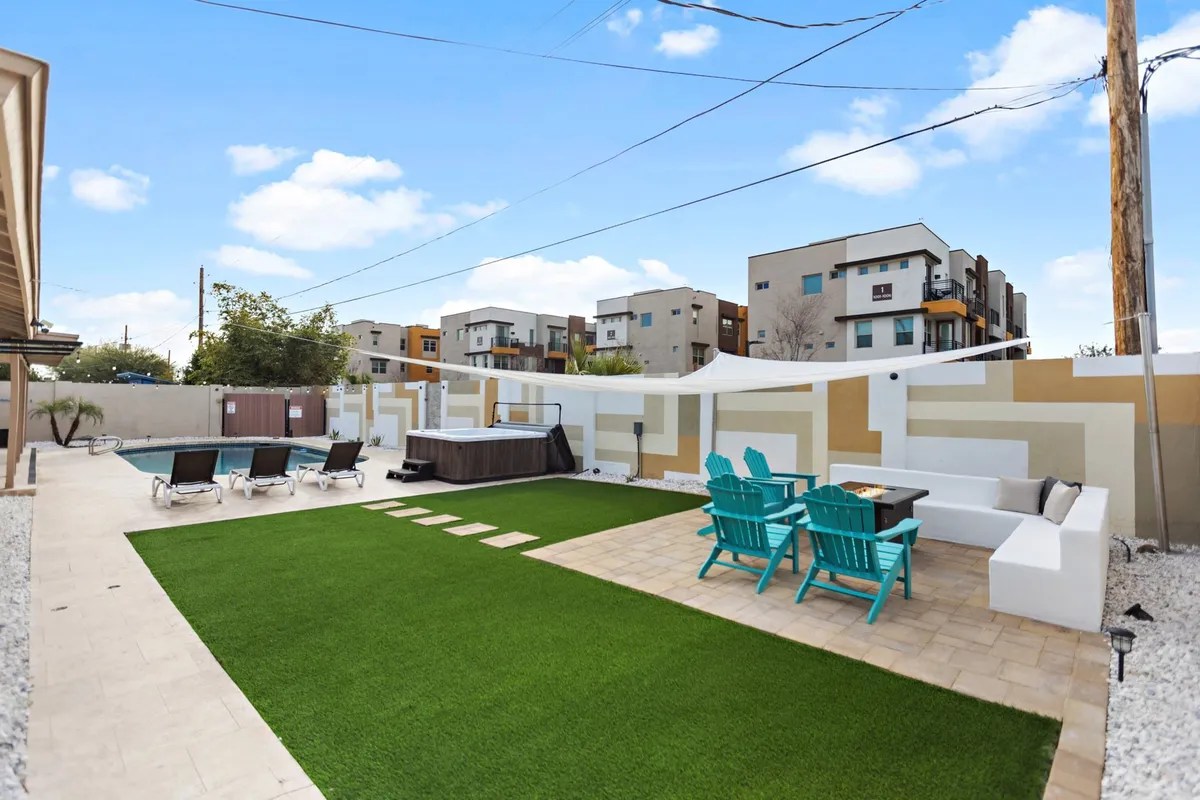 A spacious backyard featuring a lush green lawn, comfortable patio furniture, and a hot tub, all set under the open Arizona sky. The area is welcoming, with ample room for both playtime with pets and relaxation for guests.