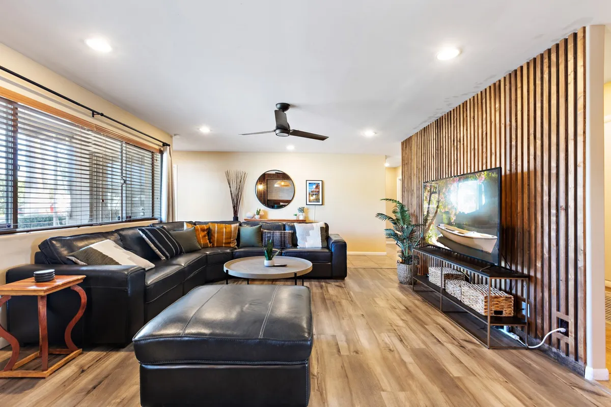 A cozy interior view with a large sectional sofa, round coffee table, wooden accent wall, TV, and decorative mirror. The space feels inviting, ideal for group hangouts, movie nights, or relaxing after energetic games.