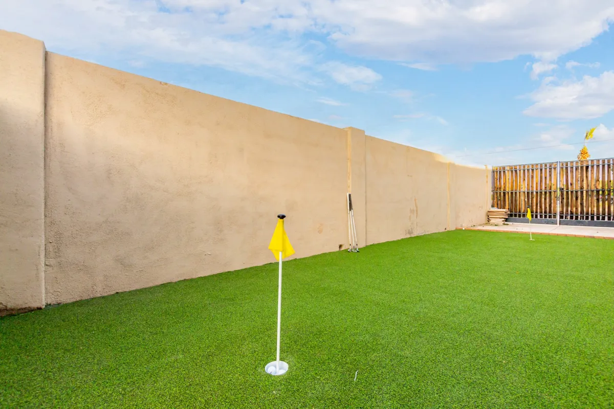 This image showcases a well-manicured backyard putting green with a smooth lawn and a yellow flag. The setting is bright and inviting, offering an ideal spot for guests to practice their golf skills right on the property.