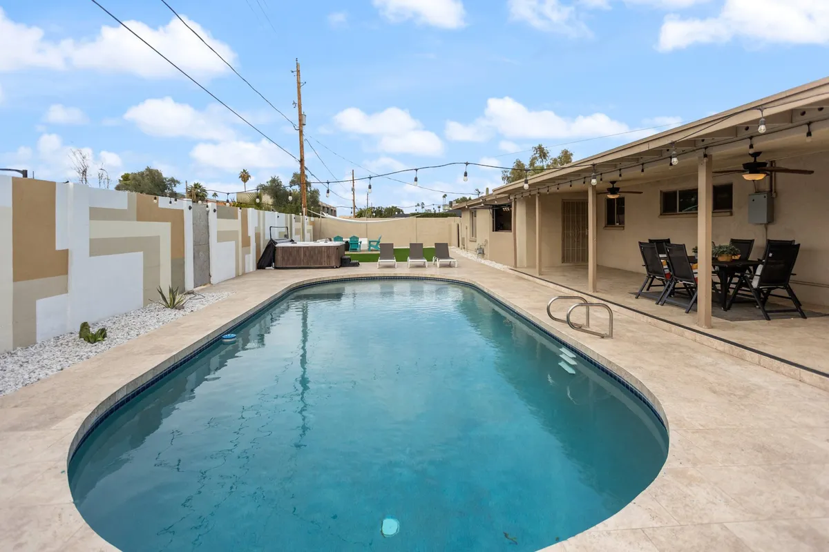 A vibrant backyard scene featuring a sparkling swimming pool surrounded by an outdoor seating area, a decorative wall, and lush landscaping. The setup is inviting for both play and relaxation, offering ample space for children to enjoy pool activities while adults supervise from nearby seating.
