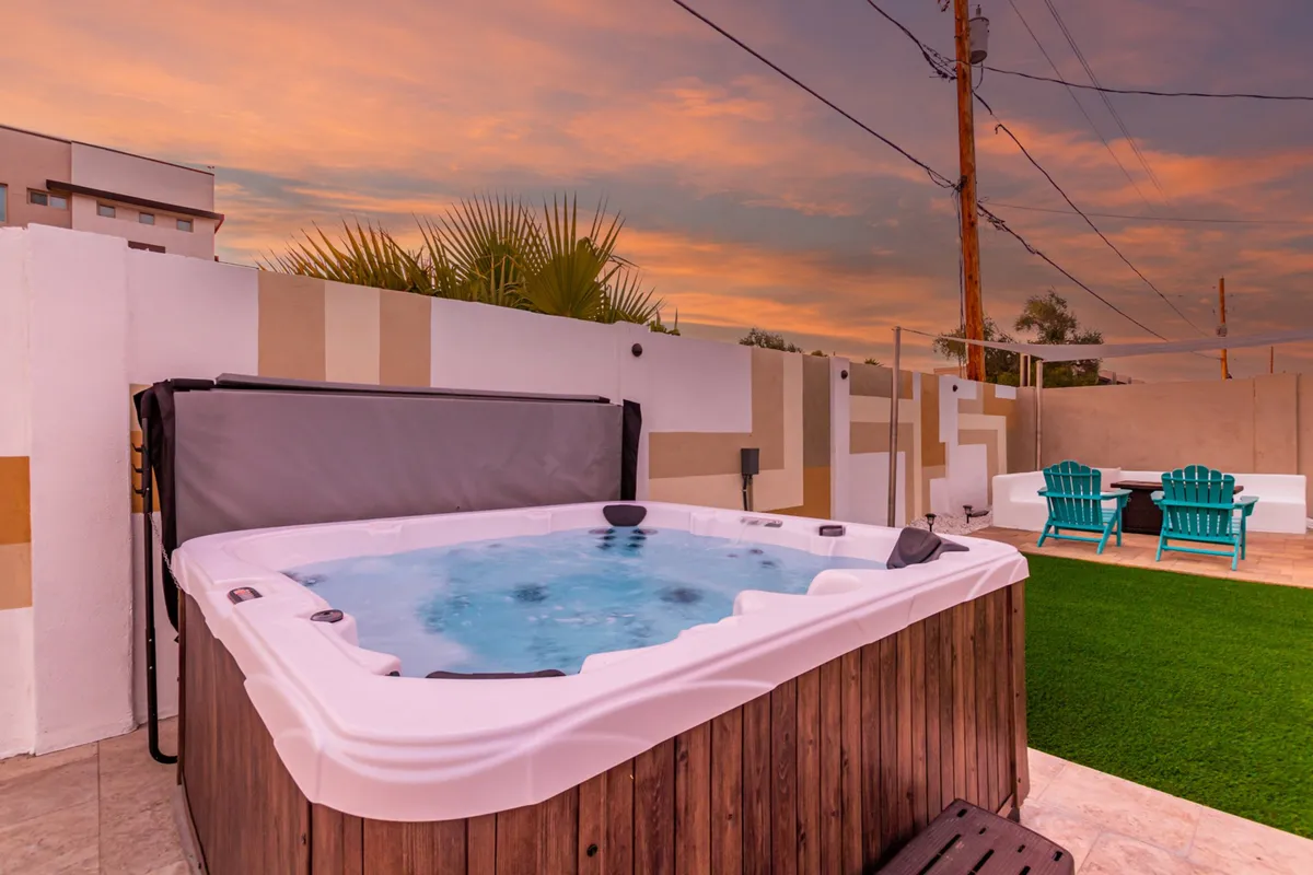 A serene backyard featuring a hot tub, comfortable lawn chairs, and a picturesque sunset sky. The setup invites guests to relax outdoors after a day of exploring the city, encouraging moments of connection and leisure under the Arizona stars.