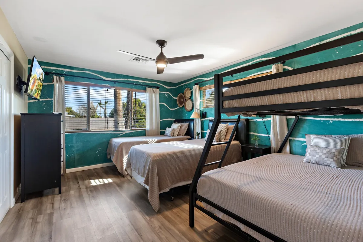A playful and comfortable bedroom featuring a bunk bed, two additional beds, a colorful mural, and a smart TV. The space is designed for versatility, accommodating family groups or friends, and encouraging both relaxation and entertainment.