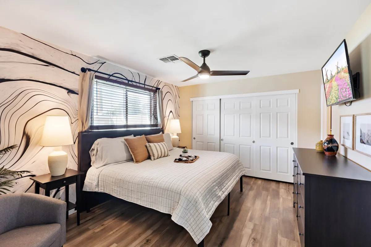 A serene bedroom with a cozy bed adorned with decorative pillows, artistic wall design, nightstands with lamps, and a dressing area complete with a mirror. The room exudes comfort and tranquility, ideal for relaxation and recharging.