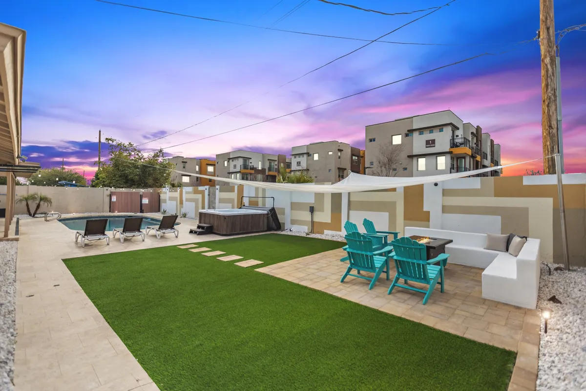 An inviting outdoor space with a vibrant green lawn, a hot tub, blue seating area, and a decorative wall, set up for socializing or unwinding after adventures. The scene feels warm, relaxed, and ideal for outdoor enjoyment with pets.